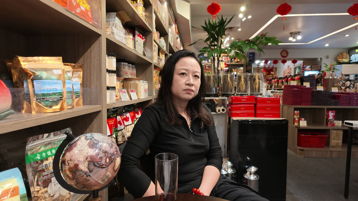 Carmen listening during an interview inside Fosetter, seated by a globe and shelves of dried goods.