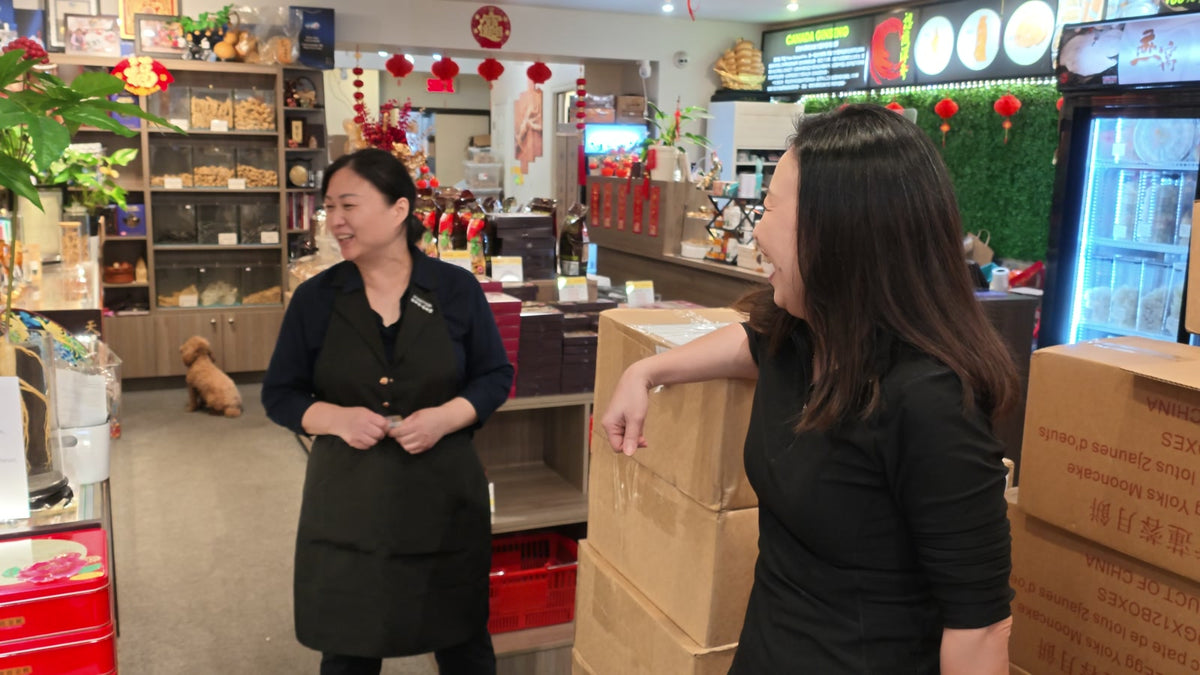 Two Fosetter team members laughing among stacked boxes inside the shop, with the shop dog in the background.