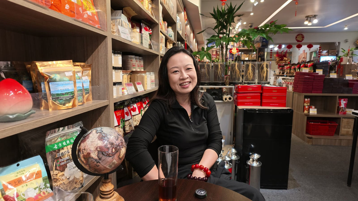 Carmen smiling at a table inside Fosetter, with shelves of ginseng and dried goods behind her.