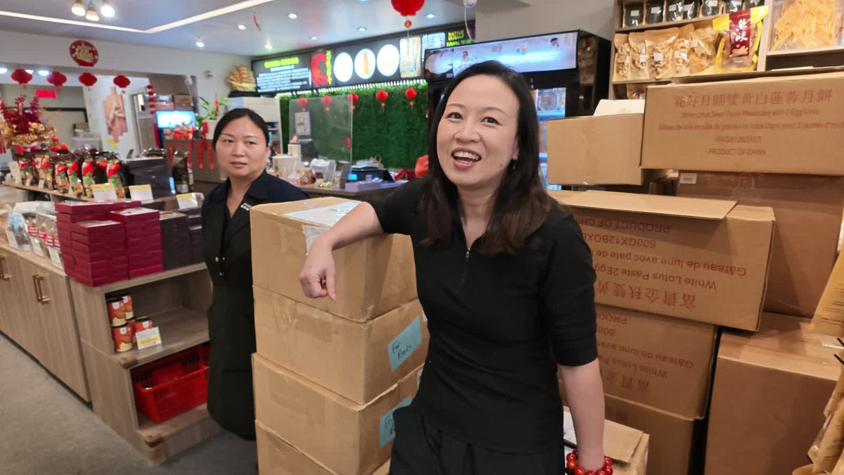 Two Fosetter staff members in the shop among stacked delivery boxes and shelves of dried goods, mid-conversation, one smiling.