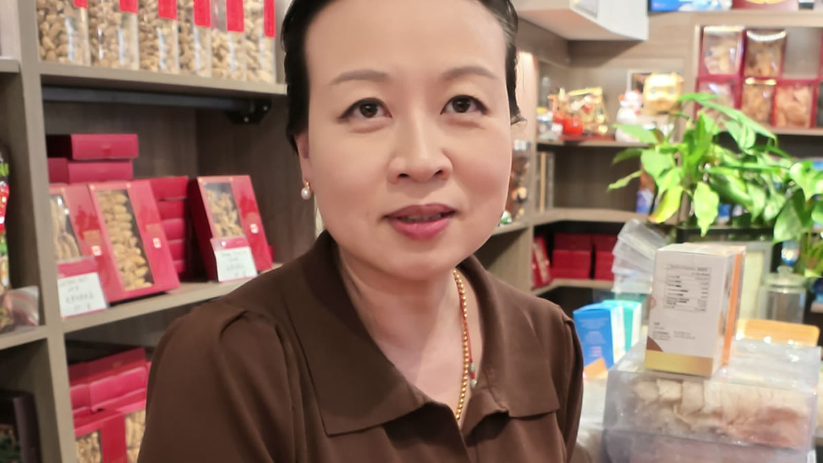 Carmen in her brown shop polo beside a tin of Xinhui chenpi at the Fosetter counter, shelves of dried goods behind her.