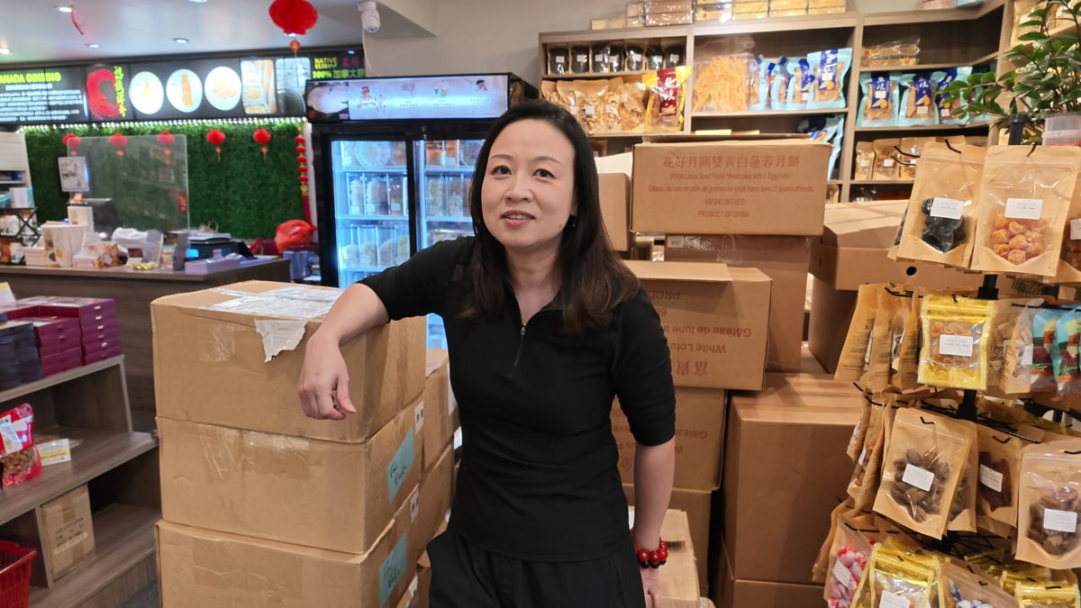 Carmen leaning on stacked delivery boxes inside Fosetter, with shelves of dried goods behind her.
