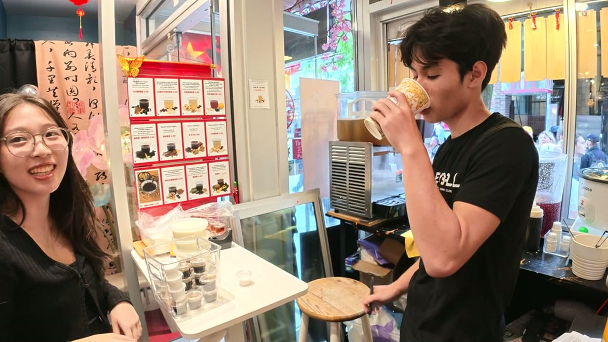 A young woman smiling and a young man drinking from a cup at Fosetter's tea window counter.